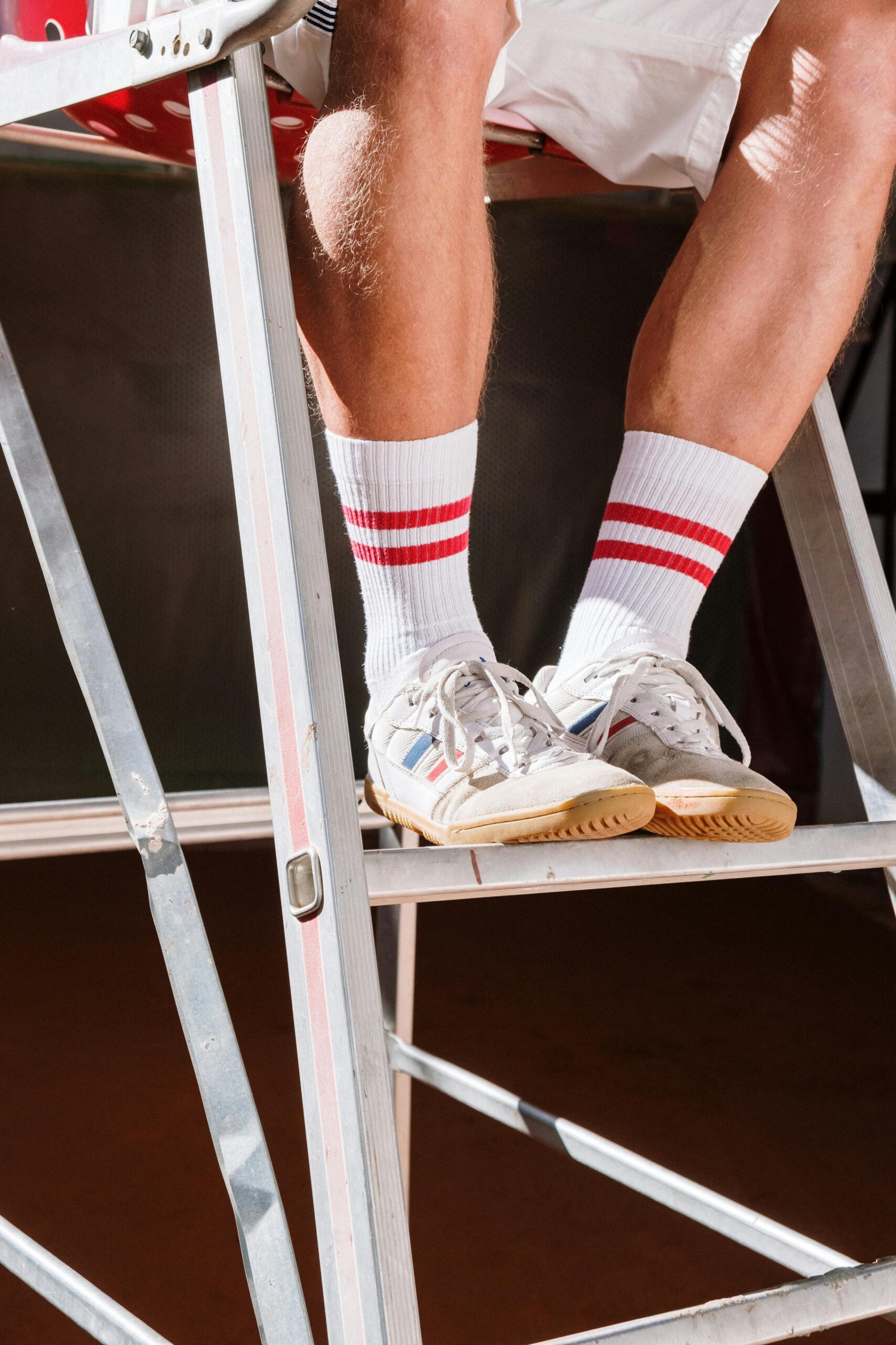 Close-up of sneakers and socks on a metal ladder in bright sunlight, emphasizing casual style.